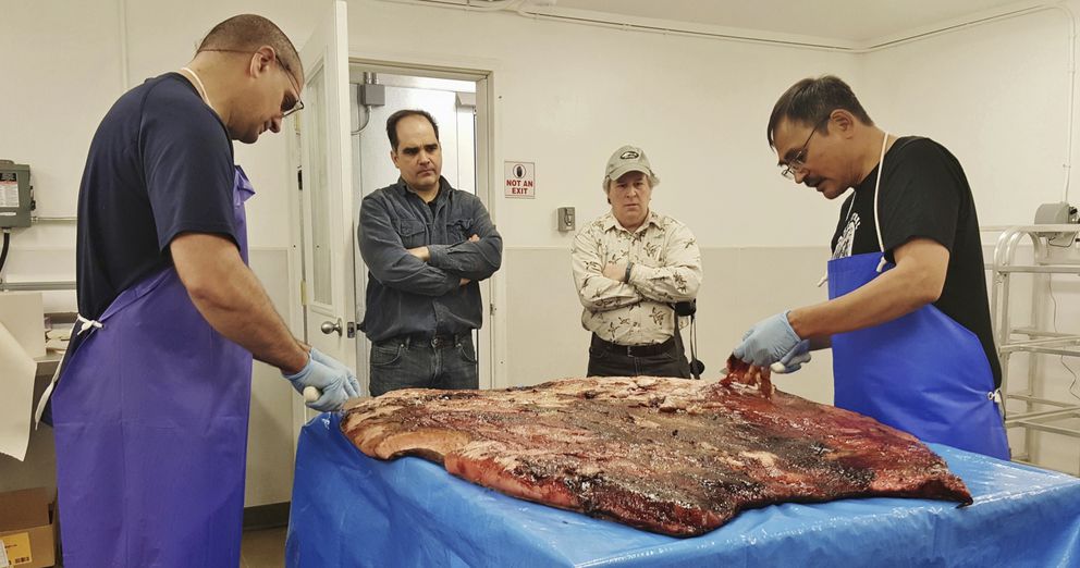 In this Oct. 28, 2016, photo provided by the Maniilaq Association, Alex Whiting, left, and Cyrus Harris, right, are observed by Chris Sannito, second from left, and Brian Himelbloom, third from left, of the Kodiak Seafood and Marine Science Center as they trim and clean seal blubber in Kotzebue. (Maniilaq Association via AP)