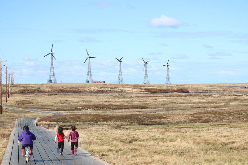 Children run along a boardwalk in Kongiganak, with the community's 475 kw wind farm in the distance. (Amanda Byrd / Alaska Center for Energy and Power