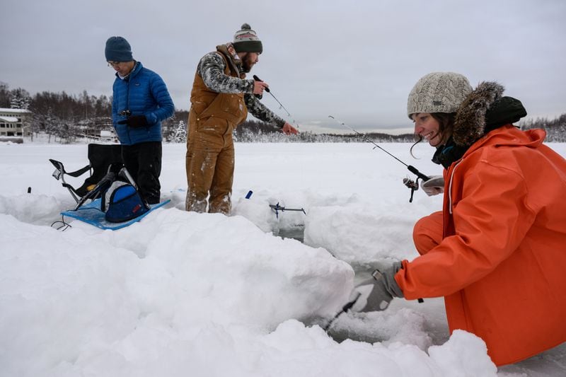 From left, Daniel Chou, Kyle Wilkinson and Elizabeth Lohman ice fish through the deep snow on Jewel Lake on December 13, 2022. Wilkinson said they had caught a couple salmon and a blackfish by mid-afternoon. (Marc Lester / ADN)