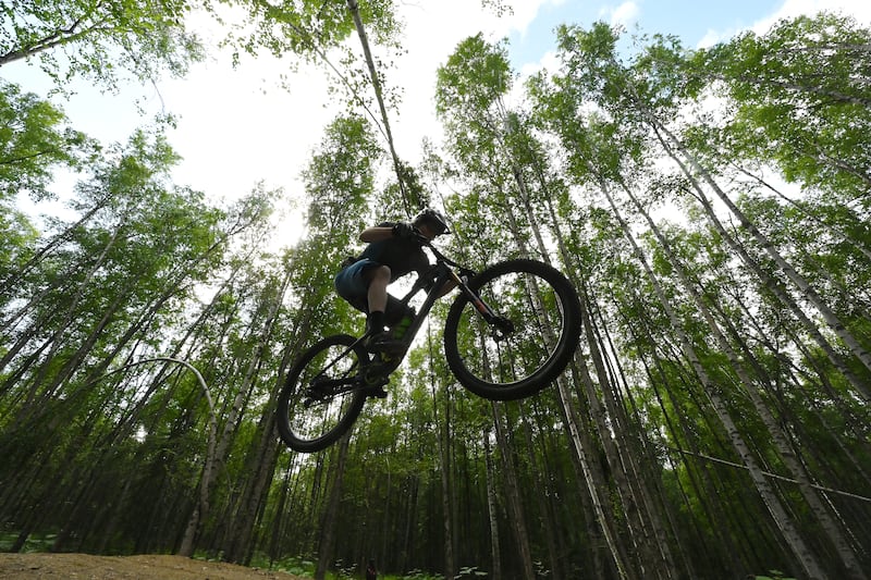James Howery launches off a jump while riding a mountain bike on the new singletrack trails that opened in Russian Jack Springs Park on Tuesday, July 9, 2024. (Bill Roth / ADN)