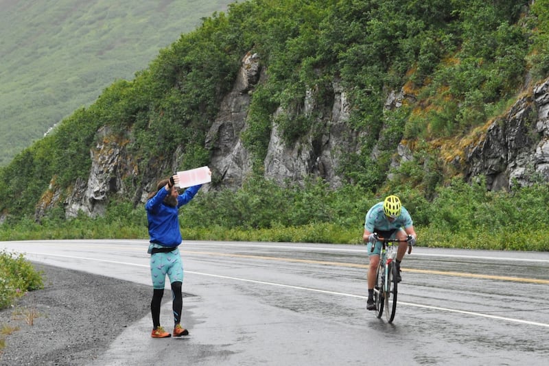 Gavin Betzelberger holds up a "Birds of Prey" sign and cheers on King Street Brewing teammate Adam Cooley while he climbs along the Richardson Highway toward Worthington Glacier during the 200-mile Fireweed bicycle race to Valdez on Saturday, July 13, 2024. (Vicky Ho / ADN)