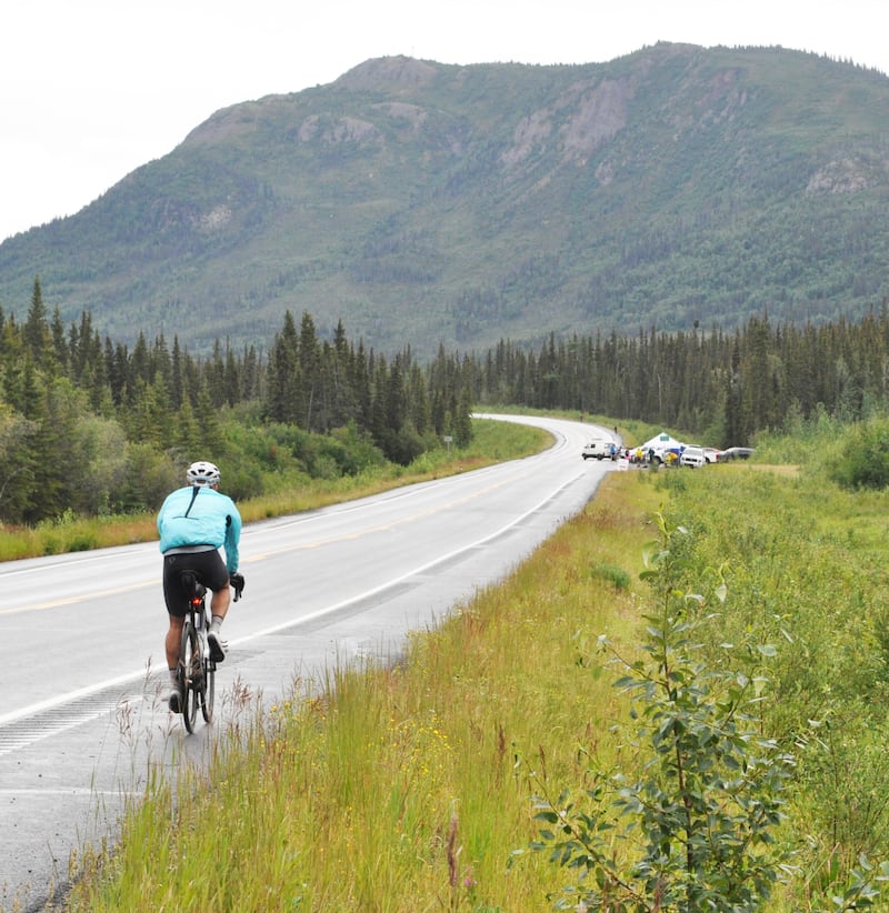 A member of the two-person "Post-Poop Zoomies" team in the 200-mile Fireweed bicycle race pedals along the Richardson Highway, receiving cheers on the approach to the Willow Creek aid station at Mile 91 on Saturday, July 13, 2024. (Vicky Ho / ADN)