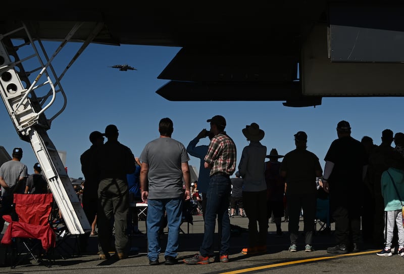 A JBER-based C-17 flies by as people find shade under another cargo plane on static display during the Arctic Thunder air show at JBER.  (Bob Hallinen Photo)
