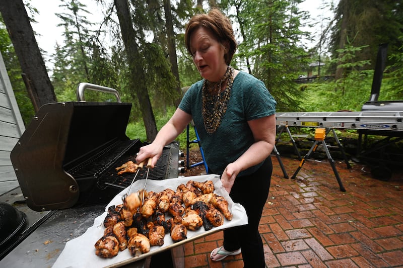 During a light rain Jennifer Mattingly pulls chicken off the grill in preparation for feeding eight Bucs players at her Hillside home. (Bill Roth / ADN) 